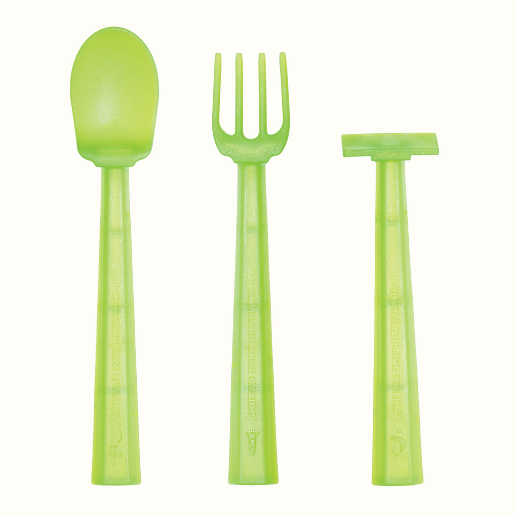 Image of the Training Utensils in a vertical position. The space alien green utensils include a pusher, fork , and spoon. There's a small detail of the big dipper on the spoon handle, a space ship on the fork handle, and a crescent moon on the pusher handle.