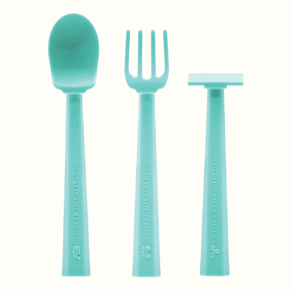 Image of the Training Utensils in a vertical position. The seafoam green utensils include a pusher, fork , and spoon. There's a small detail of a whale on the spoon handle, a crab on the fork handle, and an octopus on the pusher handle.