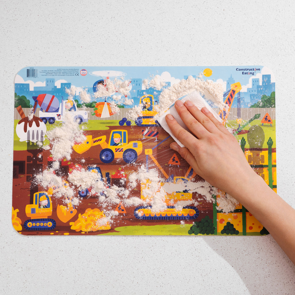 Image of the Construction Placemat covered in flour with someone using a paper towel to wipe the surface clean.