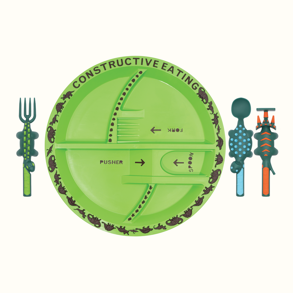 Image of the Dino Utensils and Dino Plate. The Dino Pusher is in the shape of a triceratops, the Dino Fork is in the shape of a stegosaurus, and the Dino Spoon is in the shape of an ankylosaurus. The plate is green. The utensils are located next to the plate.