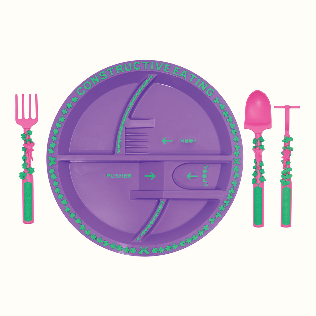 Image of the Garden Fairy Utensils and Plate. The pink utensils include a garden hoe pusher, a garden rake fork, and a garden shovel spoon. The plate is purple. The utensils are located next to the plate.