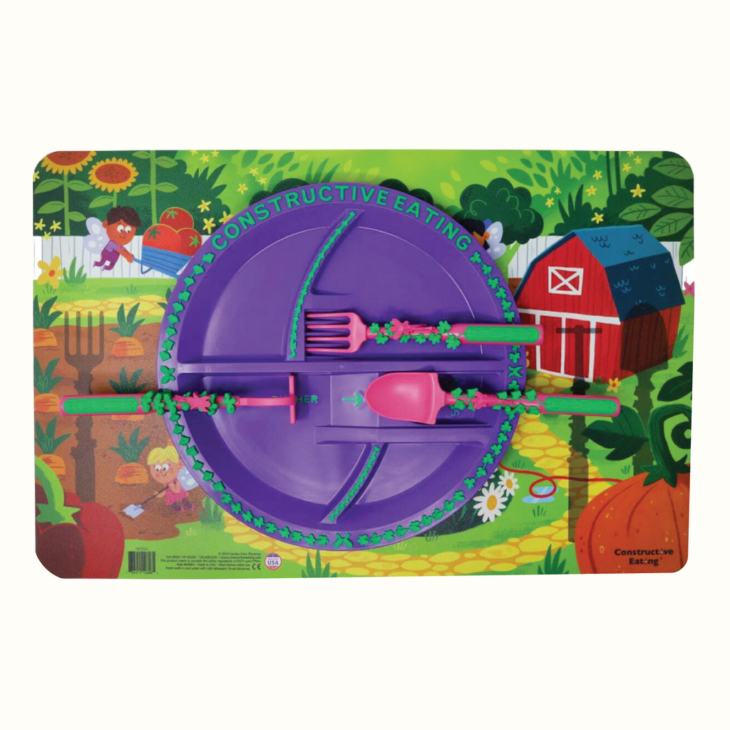 Image of the Garden Fairy Fan Bundle that includes the Garden Fairy Utensils, Plate, and Placemat. The pink utensils include a garden hoe pusher, a garden rake fork, and a garden shovel spoon. The plate is purple and the placemat illustrates a scene of fairies working in the garden. The utensils are located on their designated spots on the plate.