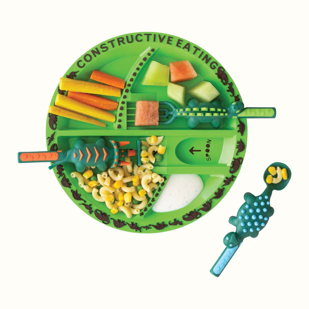 Image of the Dino Utensils and Plate. The pusher is in the shape of a triceratops, the fork in the shape of a stegosaurus, and the spoon in the shape of an ankylosaurus. The green plate is styled with melon, carrots, and pasta with peas, and carrots.