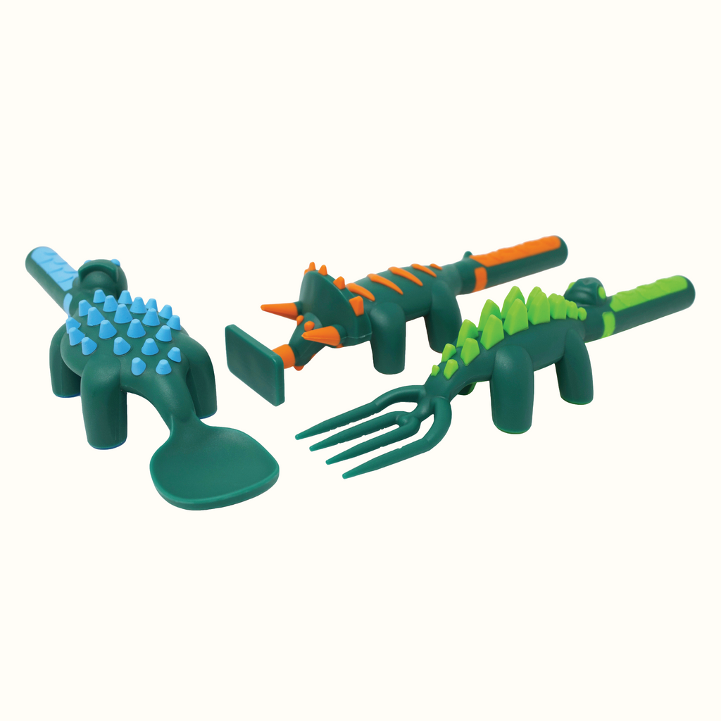 Image of the Dino Utensils angled. The Dino Pusher is in the shape of a triceratops, the Dino Fork is in the shape of a stegosaurus, and the Dino Spoon is in the shape of an ankylosaurus.